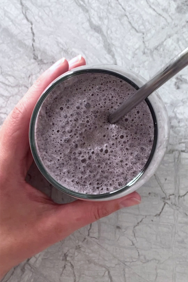 Overhead shot of the low-carb blueberry spinach smoothie in a glass with a straw atop a marble countertop.