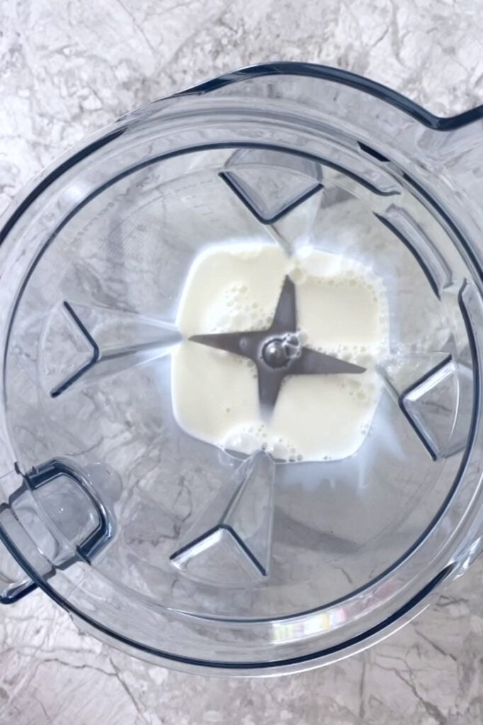 Overhead shot of a blender with coconut milk atop a marble countertop.