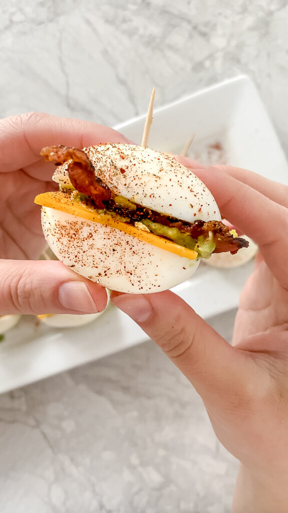 side angle shot of hands holding a breakfast egg slider garnished with paprika atop a marble countertop