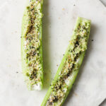 Overhead shot cucumber boats with cream cheese and mashed avocado sprinkled with Everything Bagel Seasoning atop a marble plate. The plate rests atop a marble countertop.