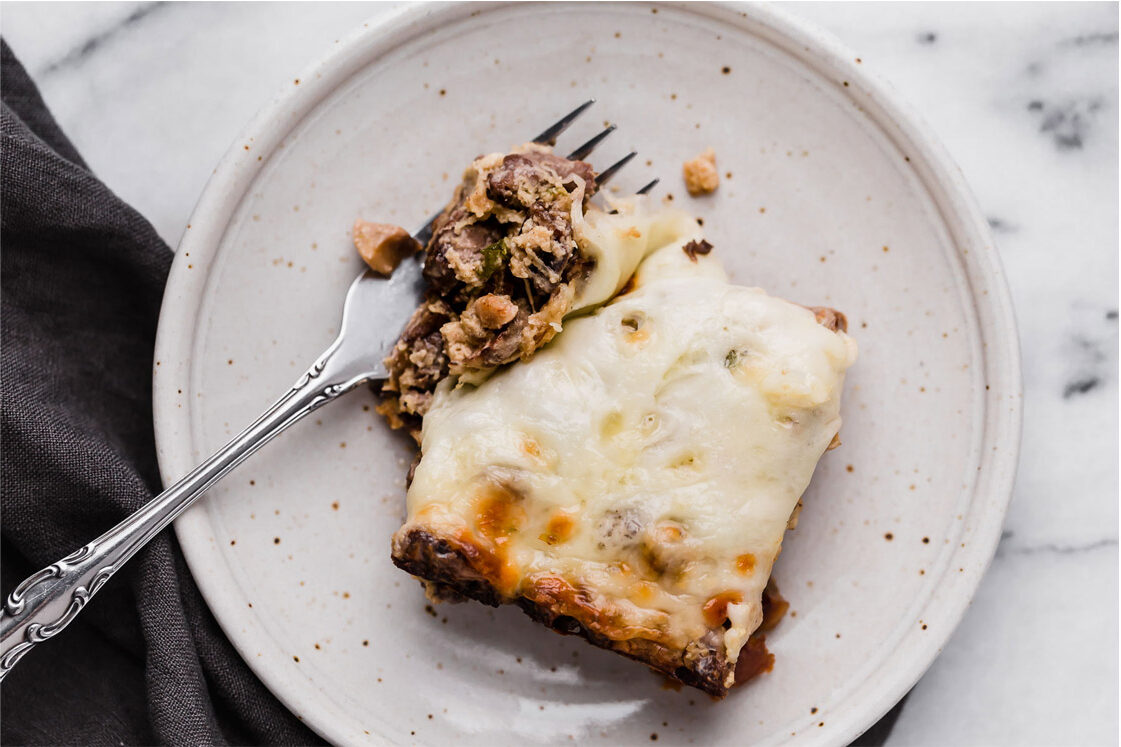 Overhead shot of a ceramic plate with a serving of the Low-Carb Philly Cheesesteak Casserole with a fork atop a marble countertop.
