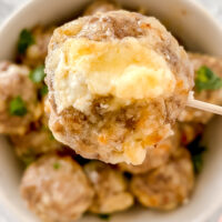 overhead shot of prepared pepper jack sausage ball on toothpick above bowl of other sausage balls atop marble countertop
