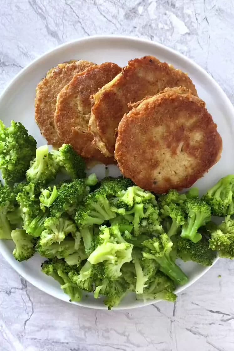 Overhead shot of the four cooked Low-Carb Chicken Patties and broccoli flowers on a small plate atop a marble countertop.