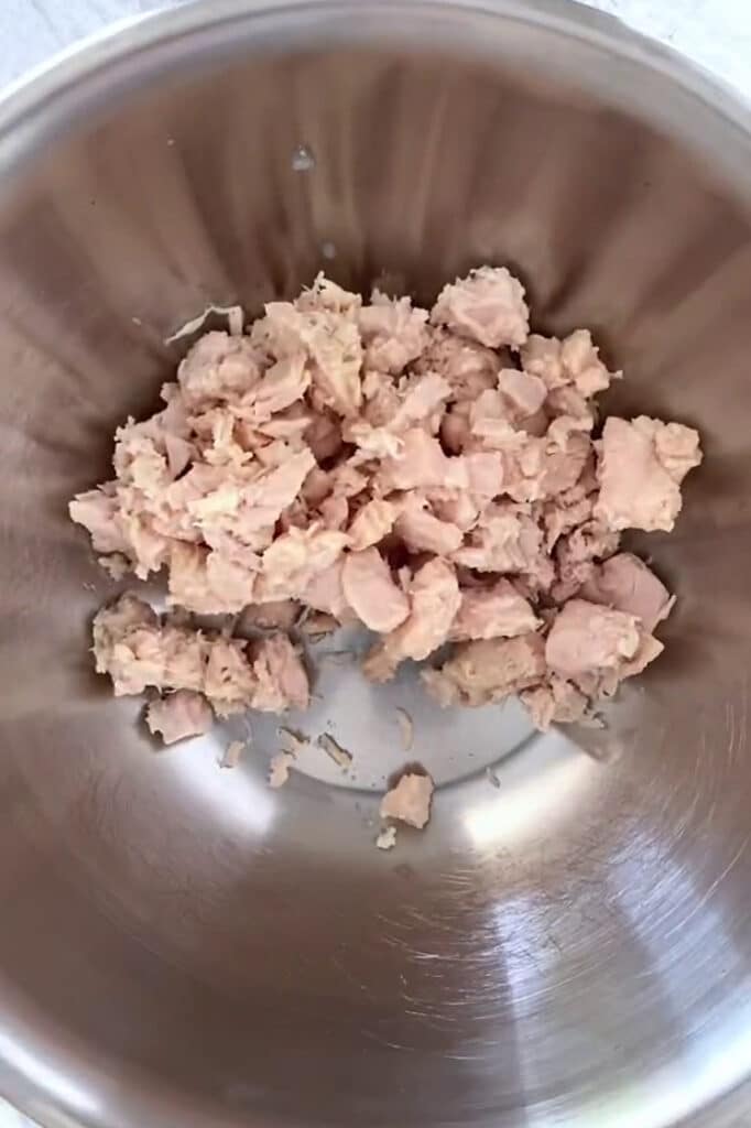 Overhead shot of drained and patted-dried canned chicken in an aluminum mixing bowl.