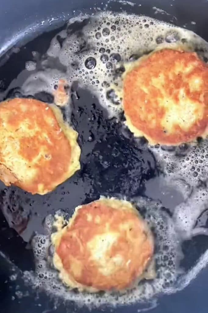 Overhead shot of three chicken patties on a large pan with avocado oil over medium heat.