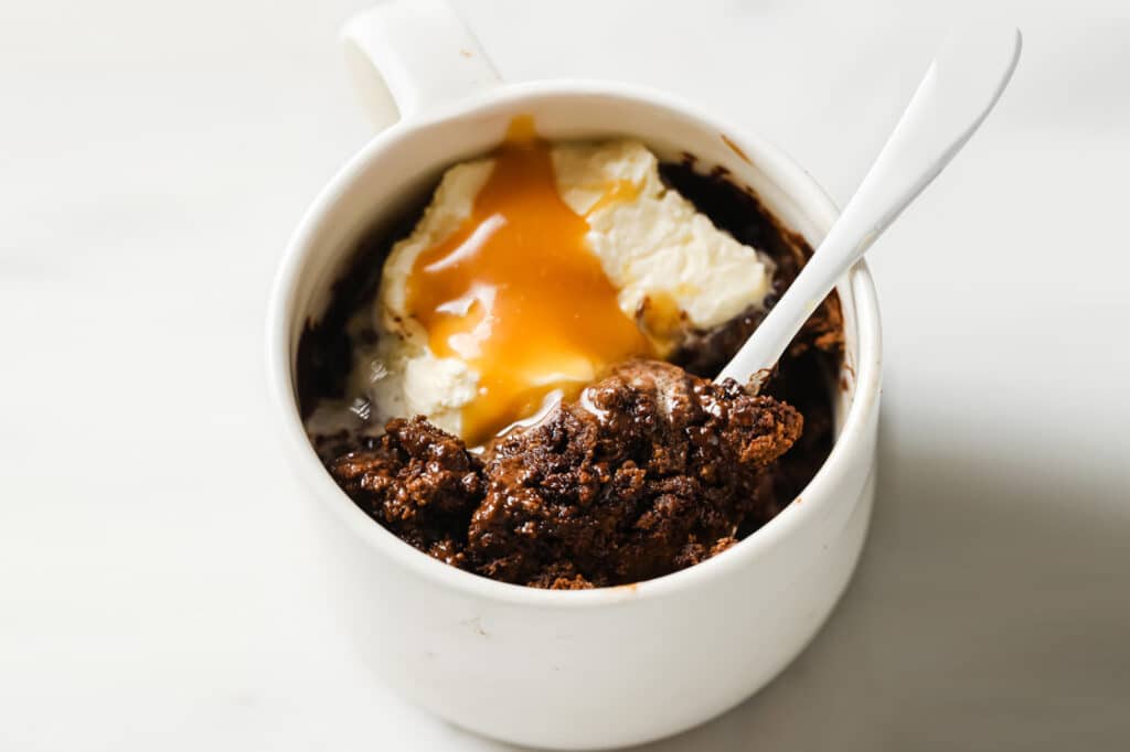 Low-carb double chocolate mug cake with ice cream and caramel in a mug with a spoon.