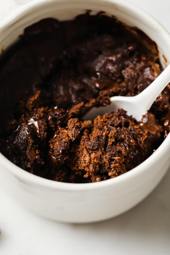 Overhead close-up shot of the Low-Carb Double Chocolate Mug Cake with a spoon in a microwavable mug atop a marble countertop.