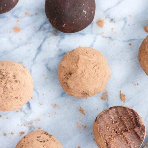 Overhead shot of chocolate Truffle Fat Bombs with one fat bomb bitten in half atop a marble countertop. In the background, you can also see a striped cloth table napkin.