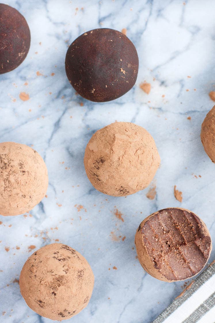 Overhead shot of chocolate Truffle Fat Bombs with one fat bomb bitten in half atop a marble countertop. In the background, you can also see a striped cloth table napkin.