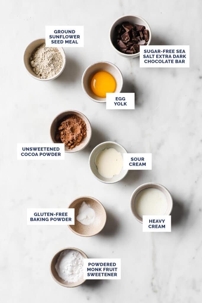 Overhead shot of labeled ingredients for mug cakes in small bowls atop a marble countertop.