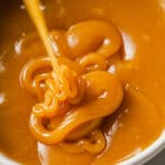 Overhead close-up shot of caramel dripping in a small bowl atop marble countertop.