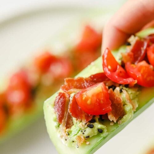 Sliced bacon and tomato cucumber boat being held in hand.