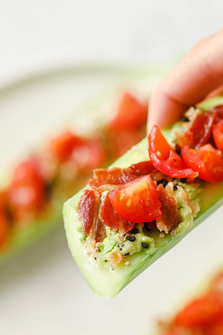Sliced bacon and tomato cucumber boat being held in hand.
