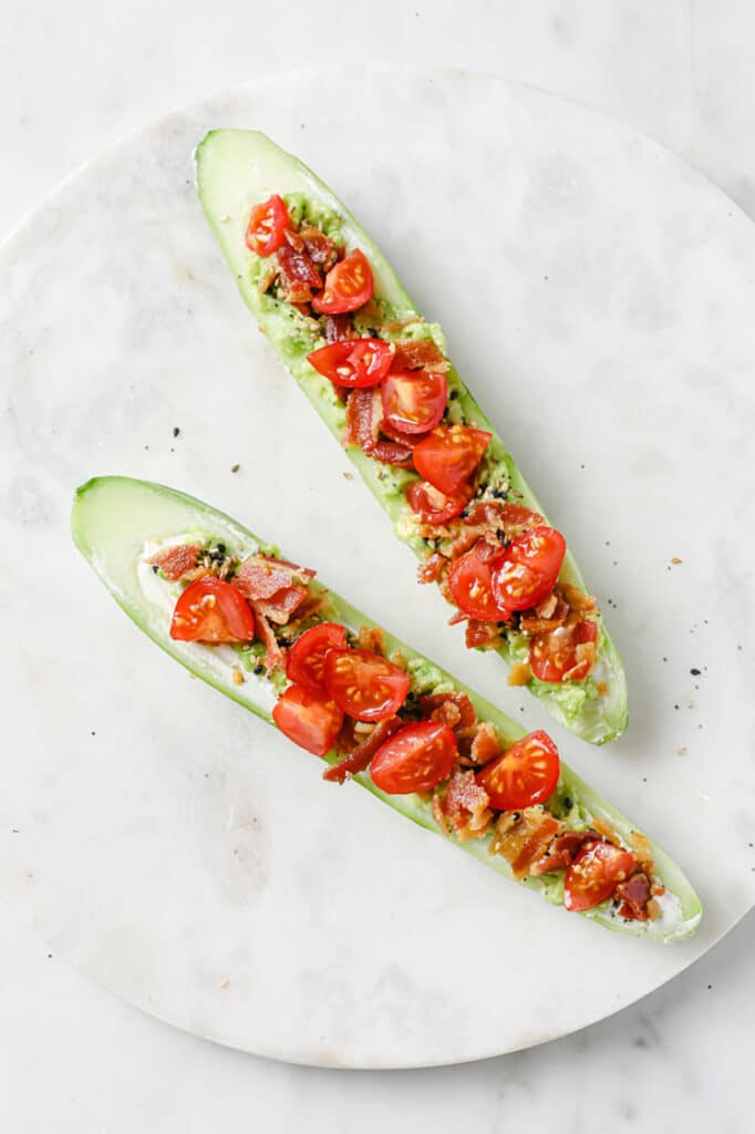 Overhead shot of two Bacon and Tomato Cucumber Boats on a round marble plate atop a marble countertop.
