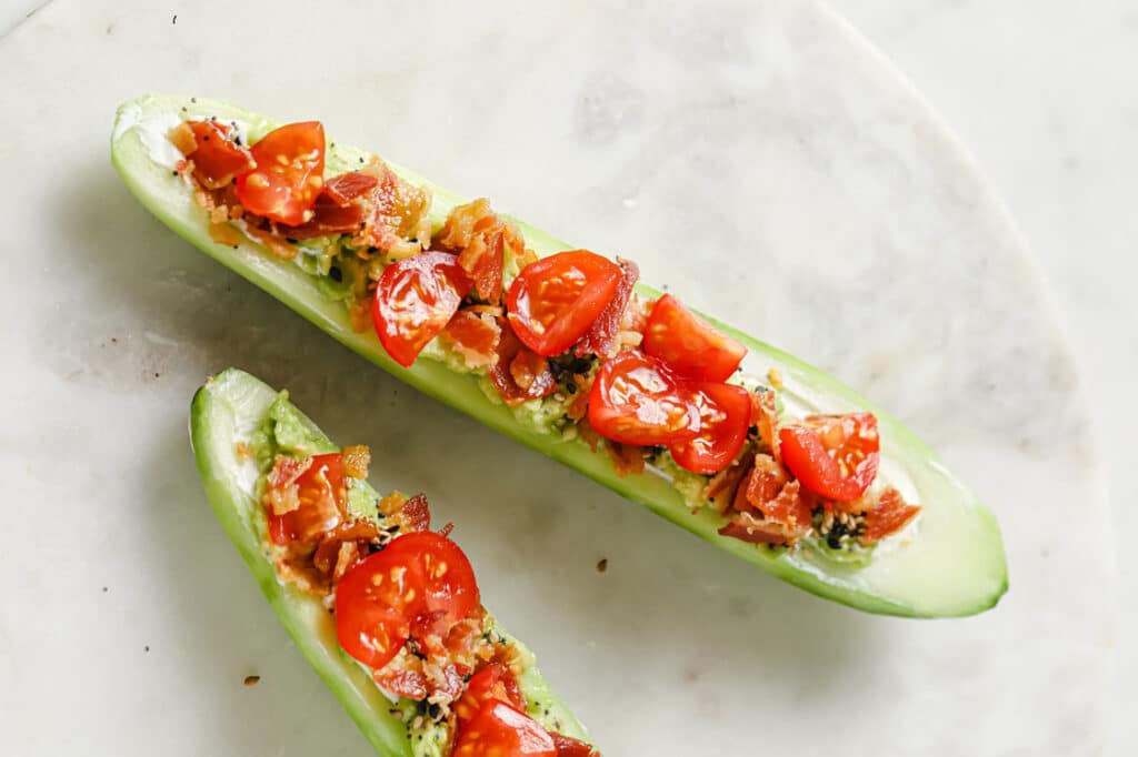 Overhead close-up shot of two Bacon and Tomato Cucumber Boats on a round marble plate atop a marble countertop.