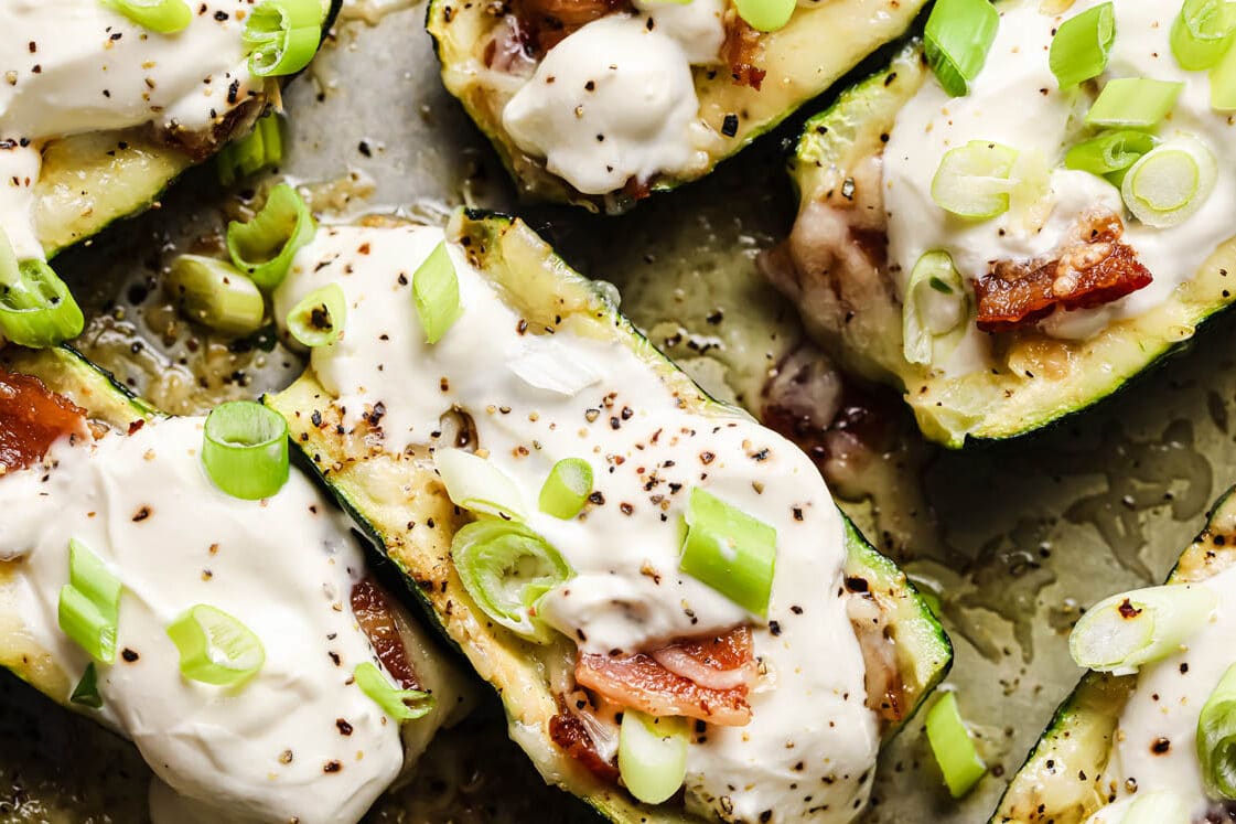 Loaded Keto Zucchini Boats garnished with a dollop of sour cream and green onions atop a baking sheet.