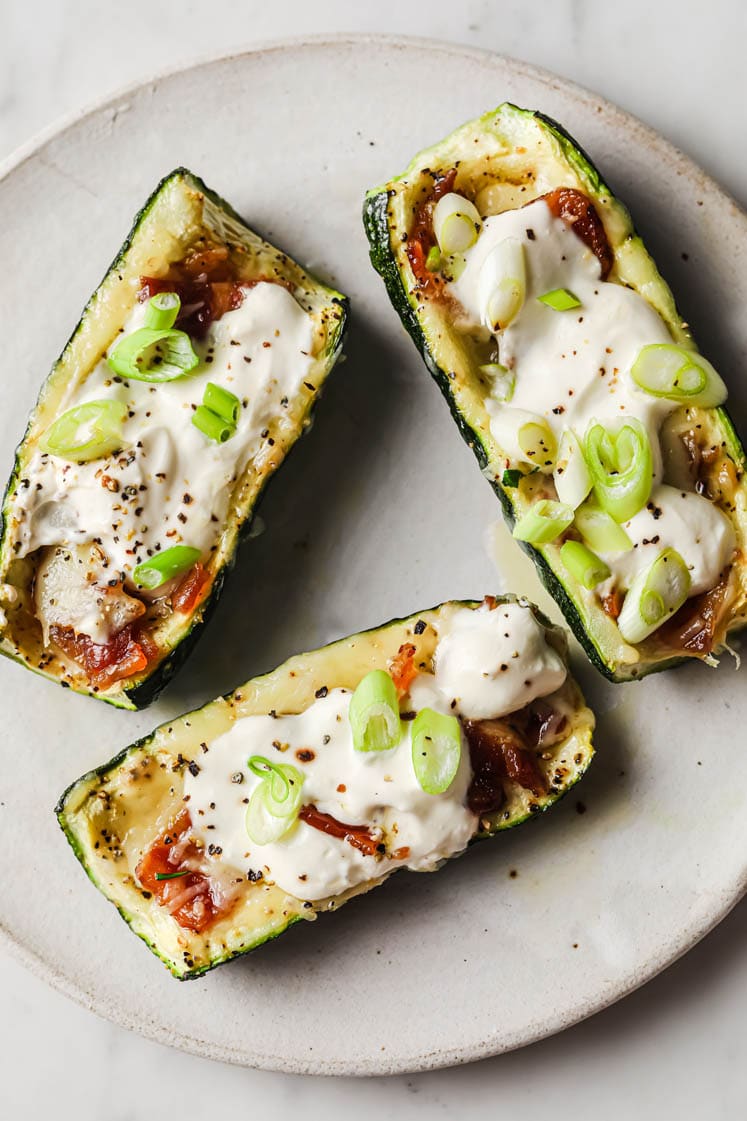 Overhead shot of 3 loaded zucchini boats atop white ceramic plate.