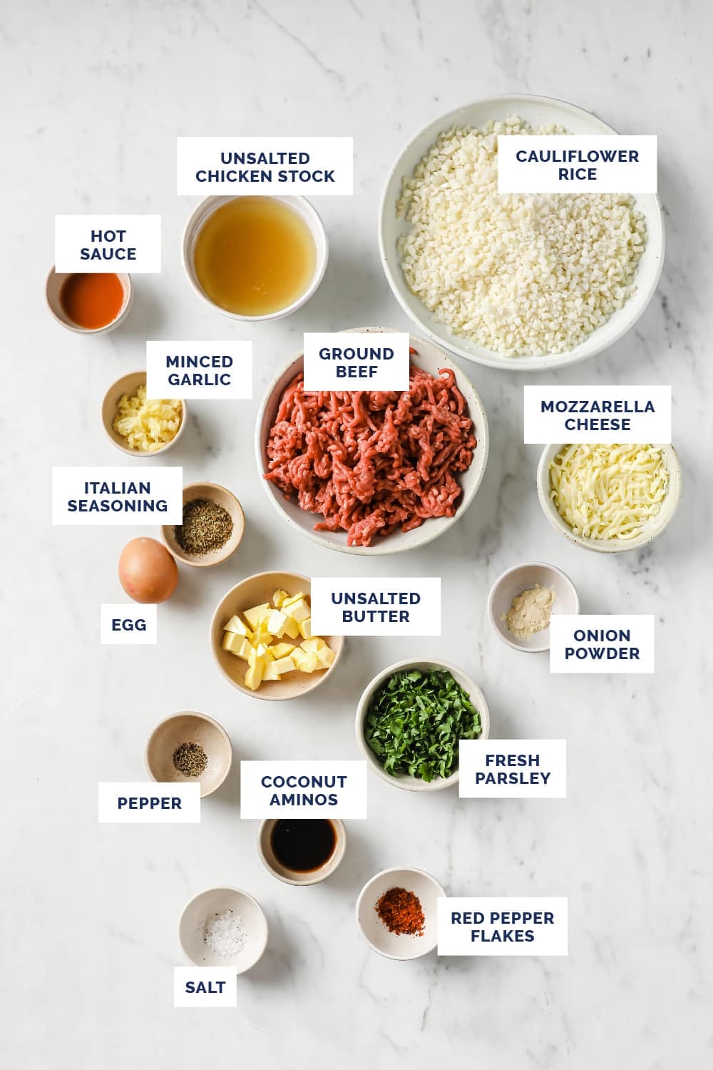 Overhead shot of Meal Prep Low-Carb Meatballs And Cauliflower Rice ingredients in bowls atop a marble countertop.
