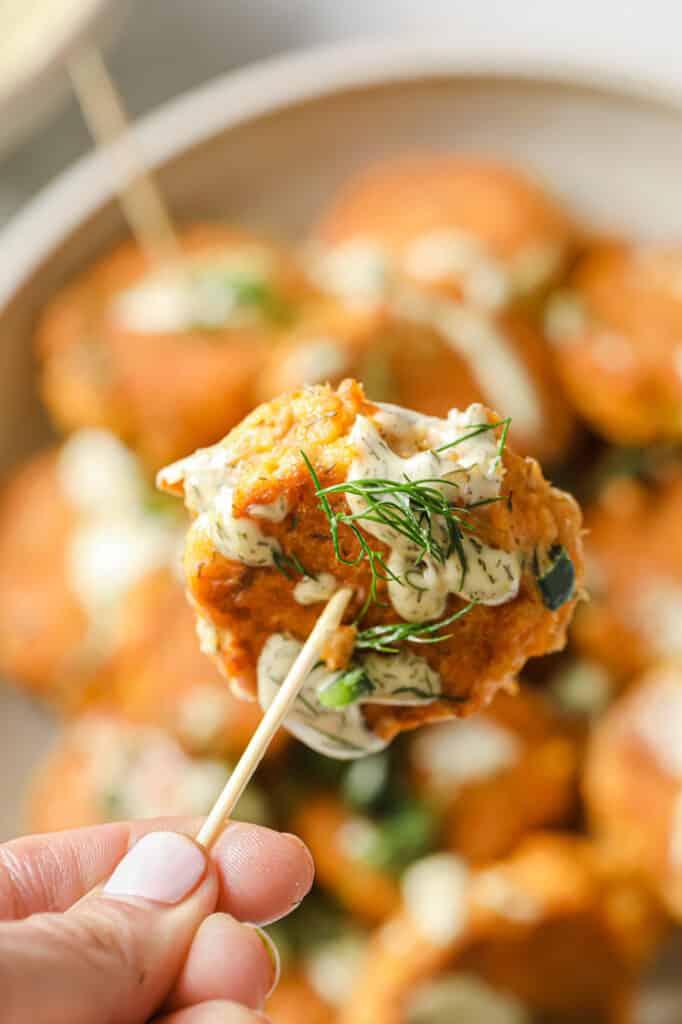Mini canned salmon patty skewered with a toothpick drizzled with aioli.