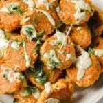 Overhead shot of a bowl with the spicy salmon poppers skewered with toothpicks, drizzled with aioli, and garnished with fresh dill and chopped jalapenos.