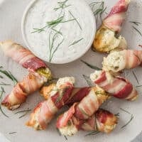 Prepared Bacon Pickle Boats Stuffed With Cream Cheese on a plate garnished with fresh dill.