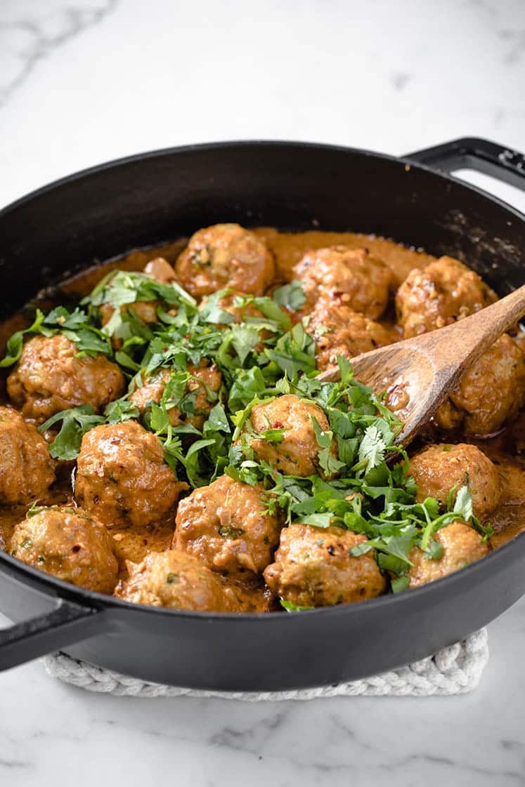 Coconut Curry Thai Turkey Meatballs garnished with fresh parsley in a cast iron skillet atop a marble counter.