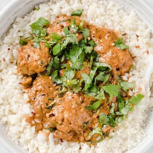 Coconut Curry Thai Turkey Meatballs garnished with fresh parsley served atop steamed cauliflower rice in a shallow bowl. The bowl rests atop a marble counter.