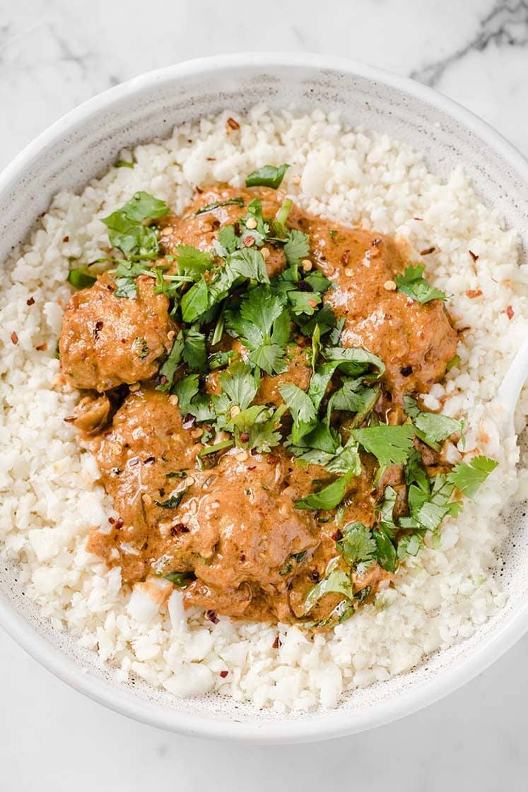 Coconut Curry Thai Turkey Meatballs garnished with fresh parsley served atop steamed cauliflower rice in a shallow bowl. The bowl rests atop a marble counter.