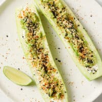 Tajin Cucumber Boats with Lime Juice and a slice of lime on a ceramic plate atop a marble countertop.