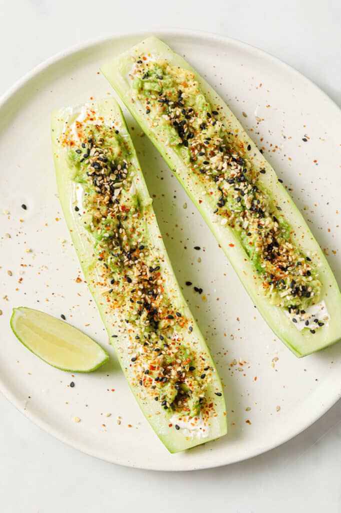 Tajin Cucumber Boats with Lime Juice and a slice of lime on a ceramic plate atop a marble countertop.