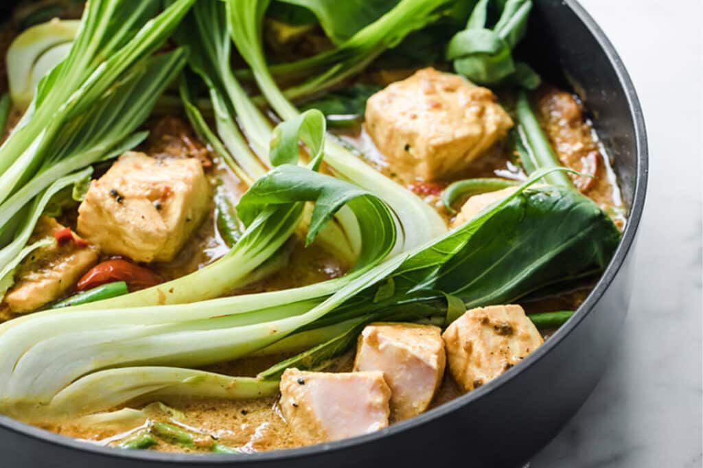 Curry Salmon With Coconut Milk And Bok Choy in a large pan atop a marble counter.