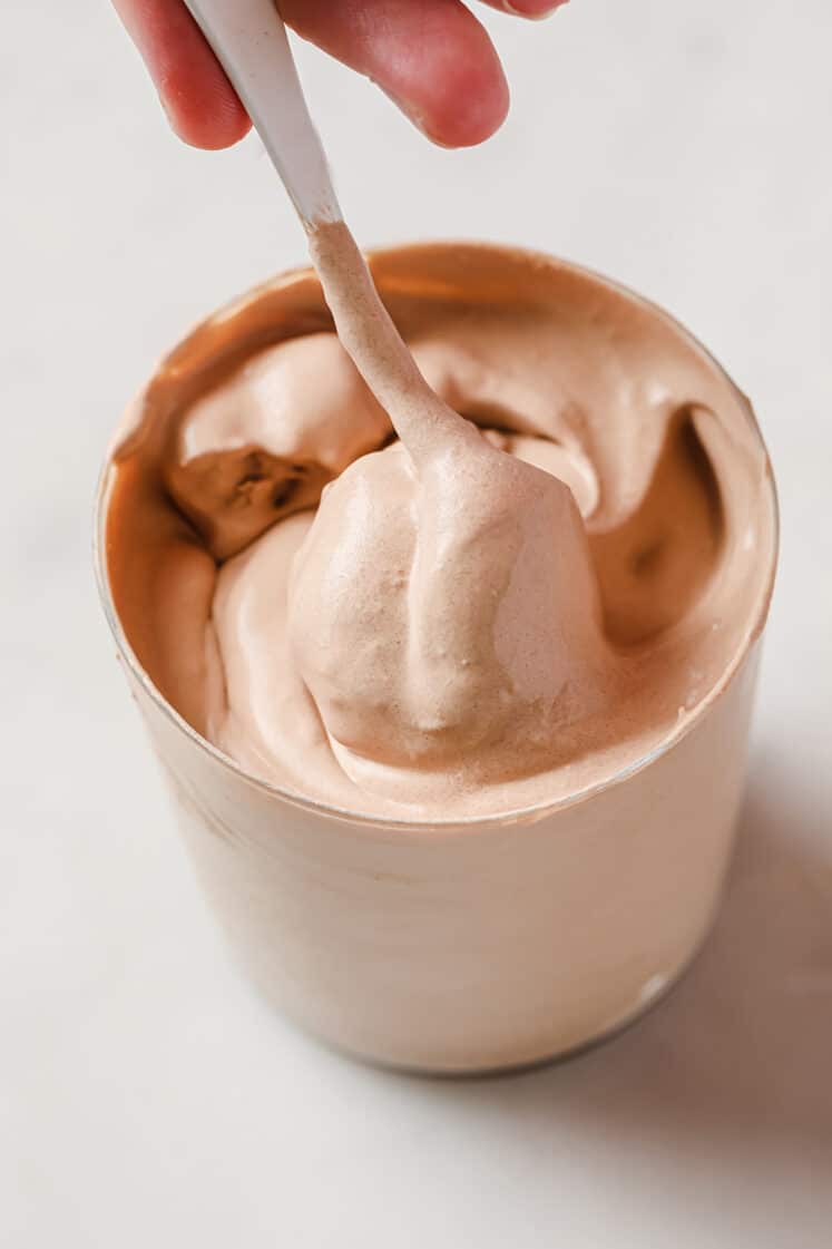 Keto Frosty in a large glass cup being stirred and spooned atop a marble countertop.