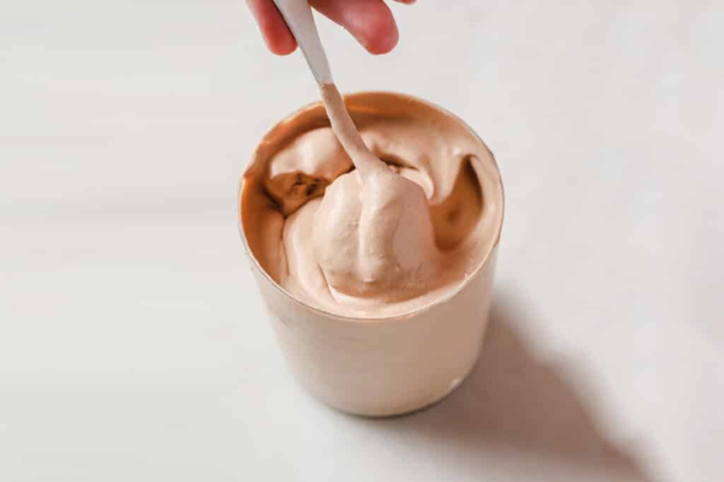 A spoon being held in a hand spooning out some chocolate ice cream.