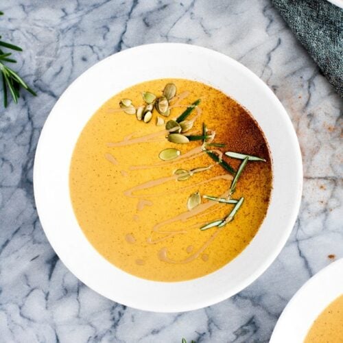 Garnished bowls of pumpkin soup on a marble countertop.