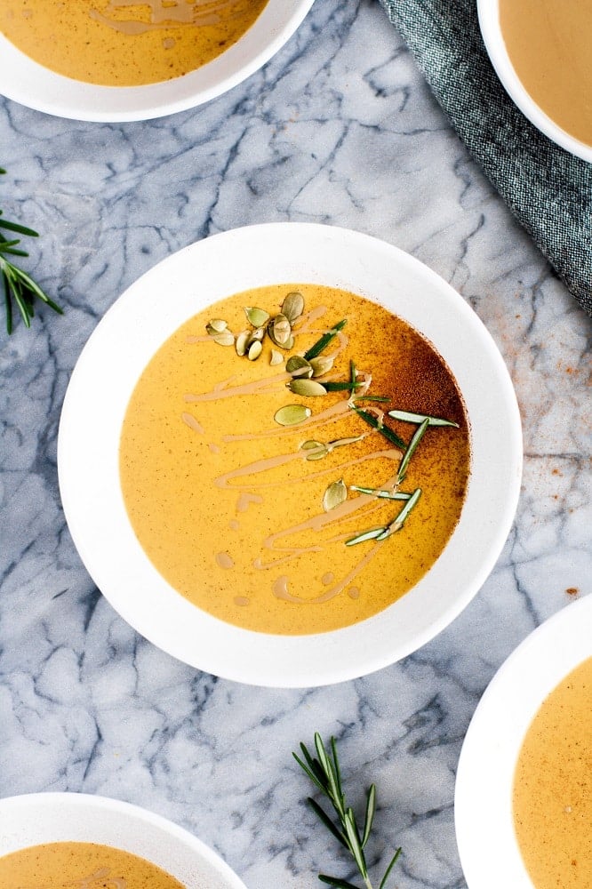 Garnished bowls of pumpkin soup on a marble countertop.