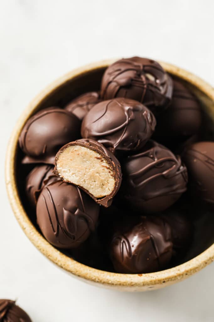 Chocolate Peanut Butter Balls with one halved ball in a bowl atop a marble counter.