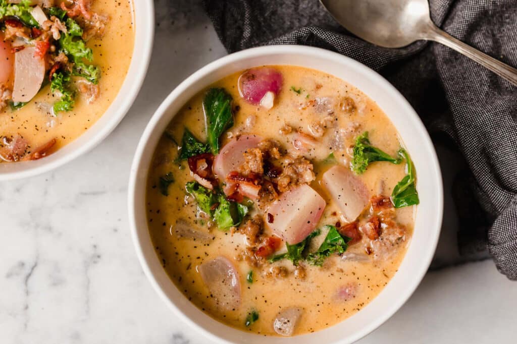 Two bowls of Keto Zuppa Toscana on a marble counter.