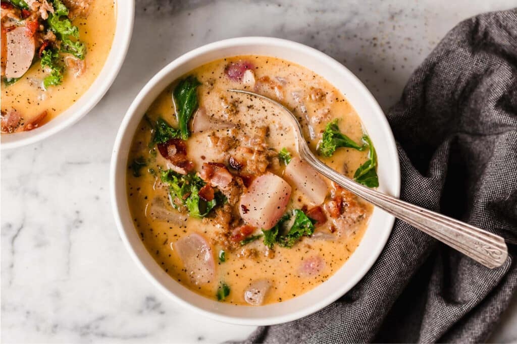 Two bowls of Keto Zuppa Toscana on a marble counter. One of the bowls has a spoon in it.