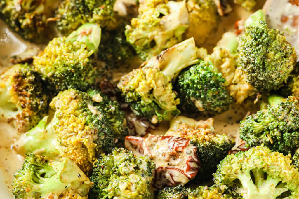 Close-up of Creamy Italian Broccoli With Sun-Dried Tomatoes garnished with black pepper in a large pan.