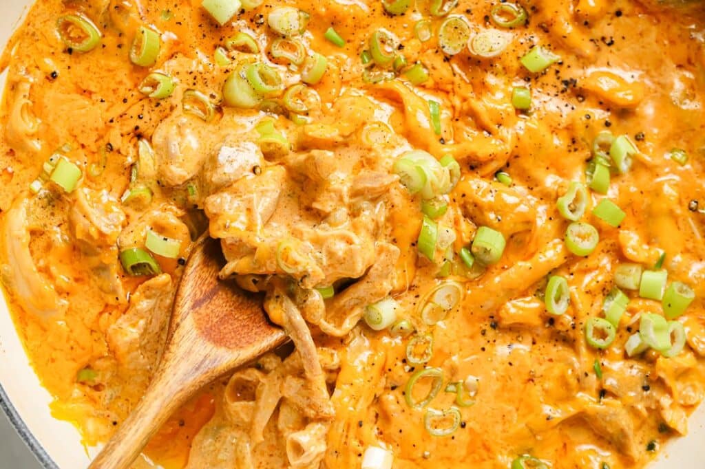 Green Chile Chicken With Leftover Shredded Chicken Thighs garnished with chopped green onions and black pepper in a cast iron skillet pan with a wooden spatula for serving.