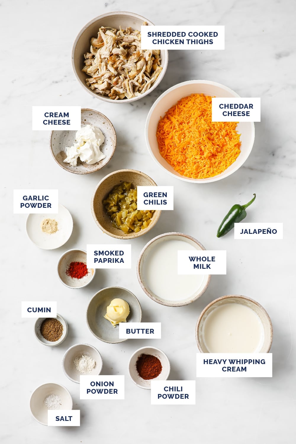 Labeled ingredients for the Green Chile Chicken With Leftover Shredded Chicken Thighs recipe in bowls atop a marble counter.