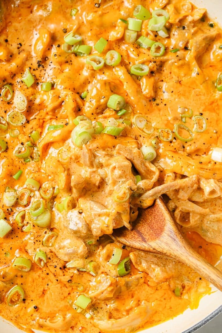 Green Chile Chicken With Leftover Shredded Chicken Thighs garnished with chopped green onions and black pepper in a cast iron skillet pan with a wooden spatula for serving.
