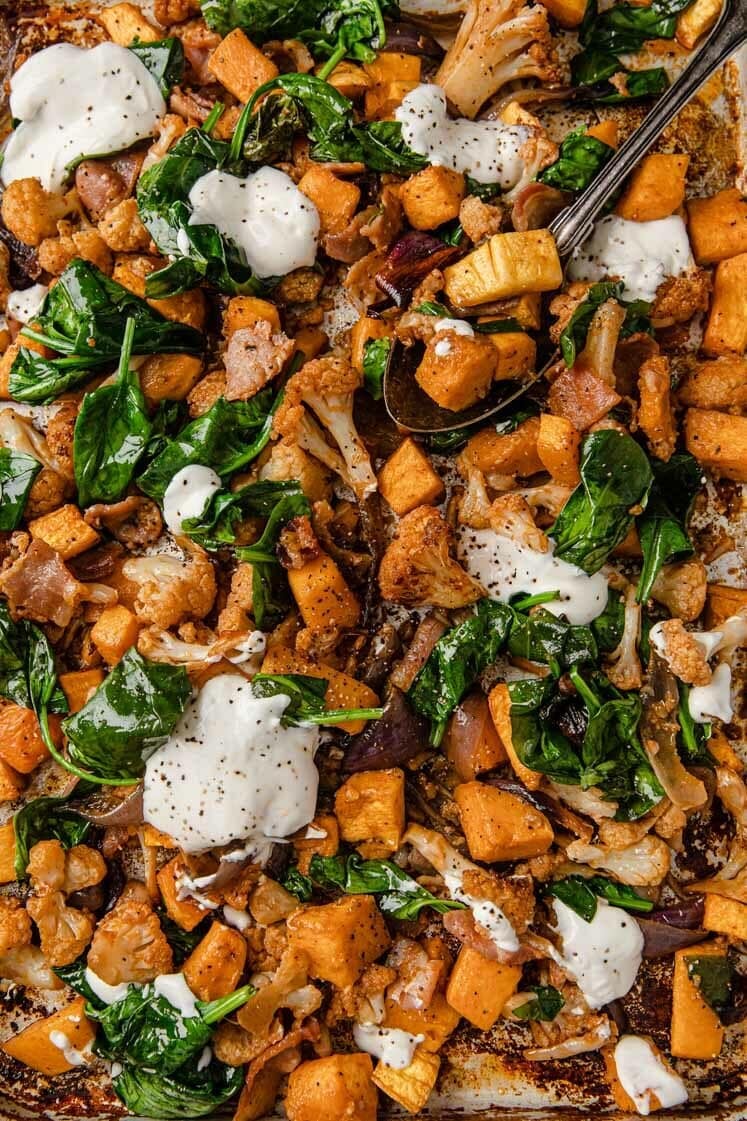 Close-up of Roasted Cubed Butternut Squash With Cauliflower And Bacon garnished with sour cream.