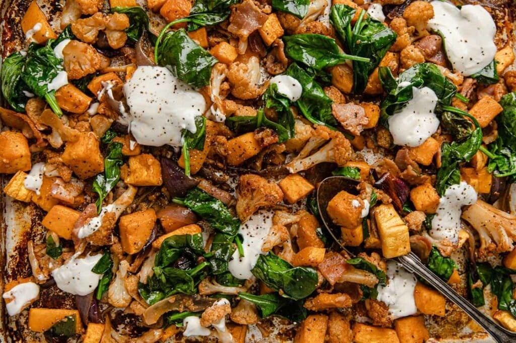 Close-up of Roasted Cubed Butternut Squash With Cauliflower And Bacon garnished with sour cream.