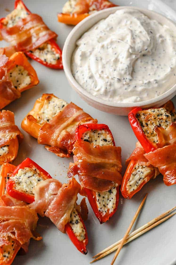 Bacon Wrapped Mini Peppers on a plate with a bowl of the Everything Bagel Dip.