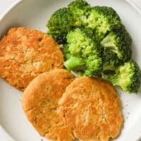 Canned Chicken Patties and steamed broccoli florets garnished with freshly cracked black pepper on a plate atop a marble counter.