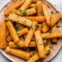 Golden Jicama Fries garnished with freshly chopped parsley on a parchment paper-lined plate atop a marble counter.