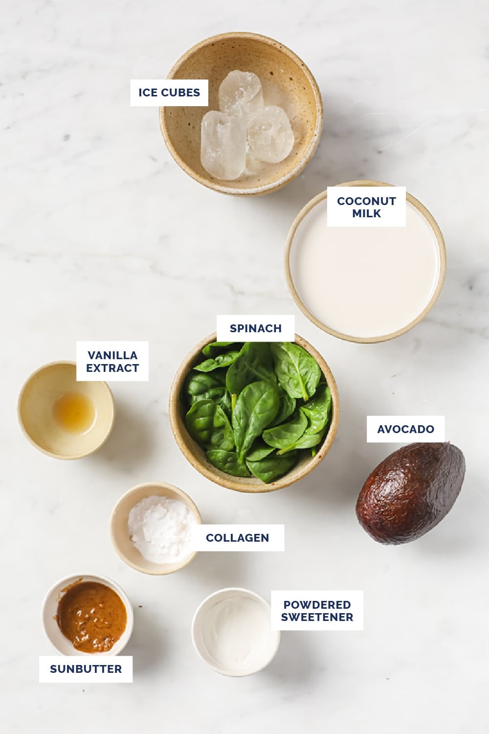 Labeled ingredients for the green smoothie recipe in bowls on a marble counter.