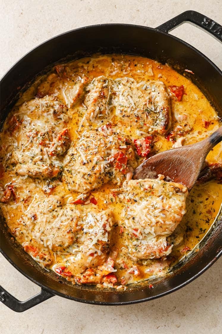 Creamy sun dried tomato chicken with a wooden spatula on a cast-iron skillet.