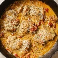 Creamy sun dried tomato chicken thighs in a cast-iron skillet atop a marble countertop.